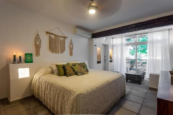 Une chambre avec un grand lit, une petite table et une vue sur l’extérieur par une fenêtre.