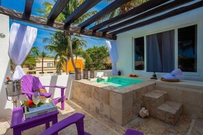Un espace extérieur privé comprenant un jacuzzi, des chaises violettes et un banc en pierre.