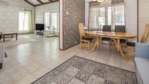 Uma sala de estar espaçosa, com teto alto, uma área de jantar com mesa e cadeiras de madeira, e uma televisão no canto.
