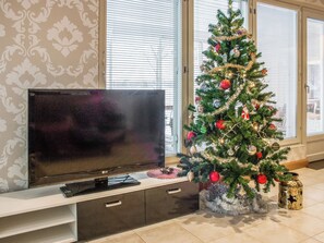A living room with a television on a stand, a Christmas tree, and a window with blinds.