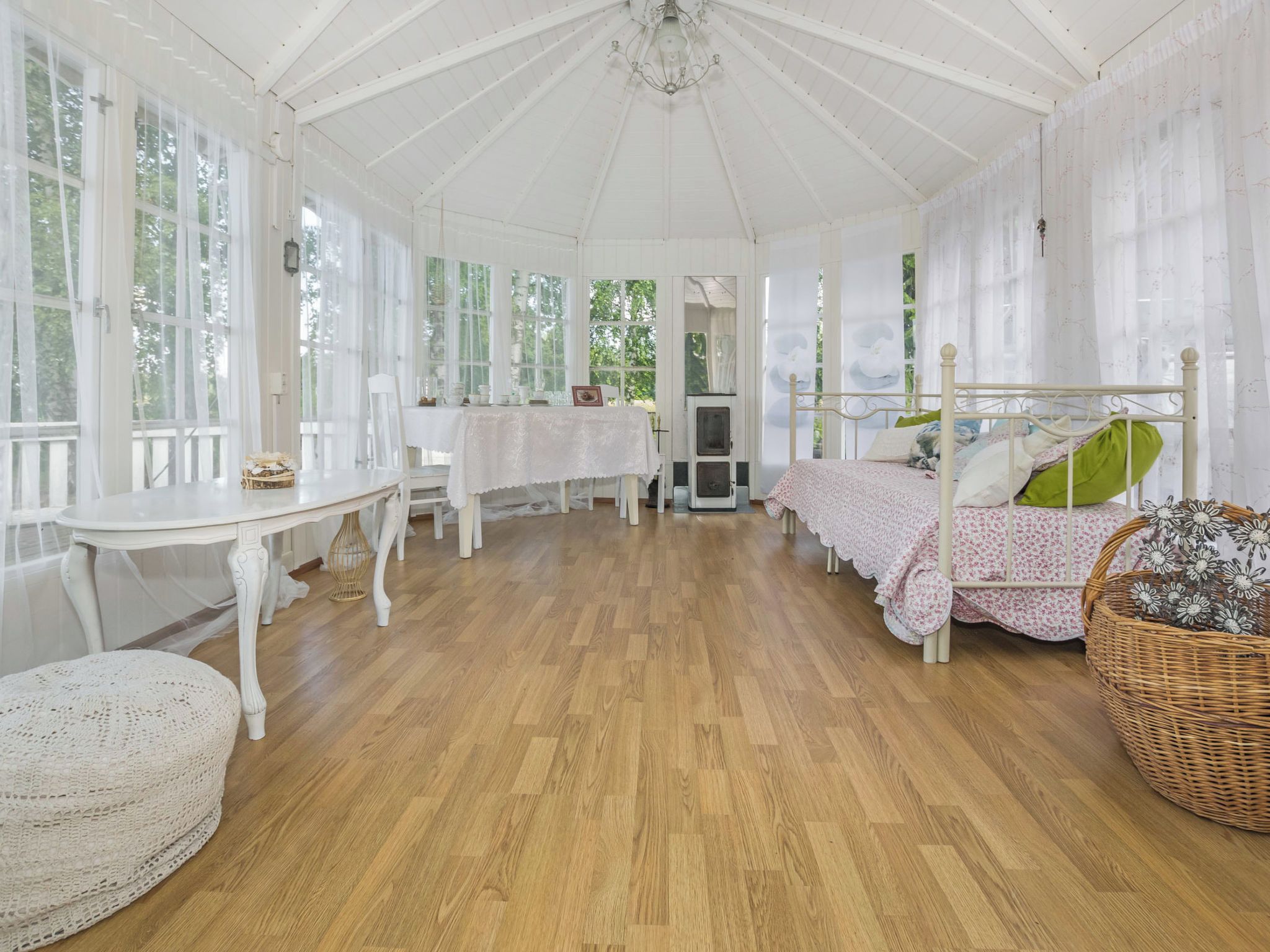 A conservatory with a wooden floor, white furniture, and large windows.