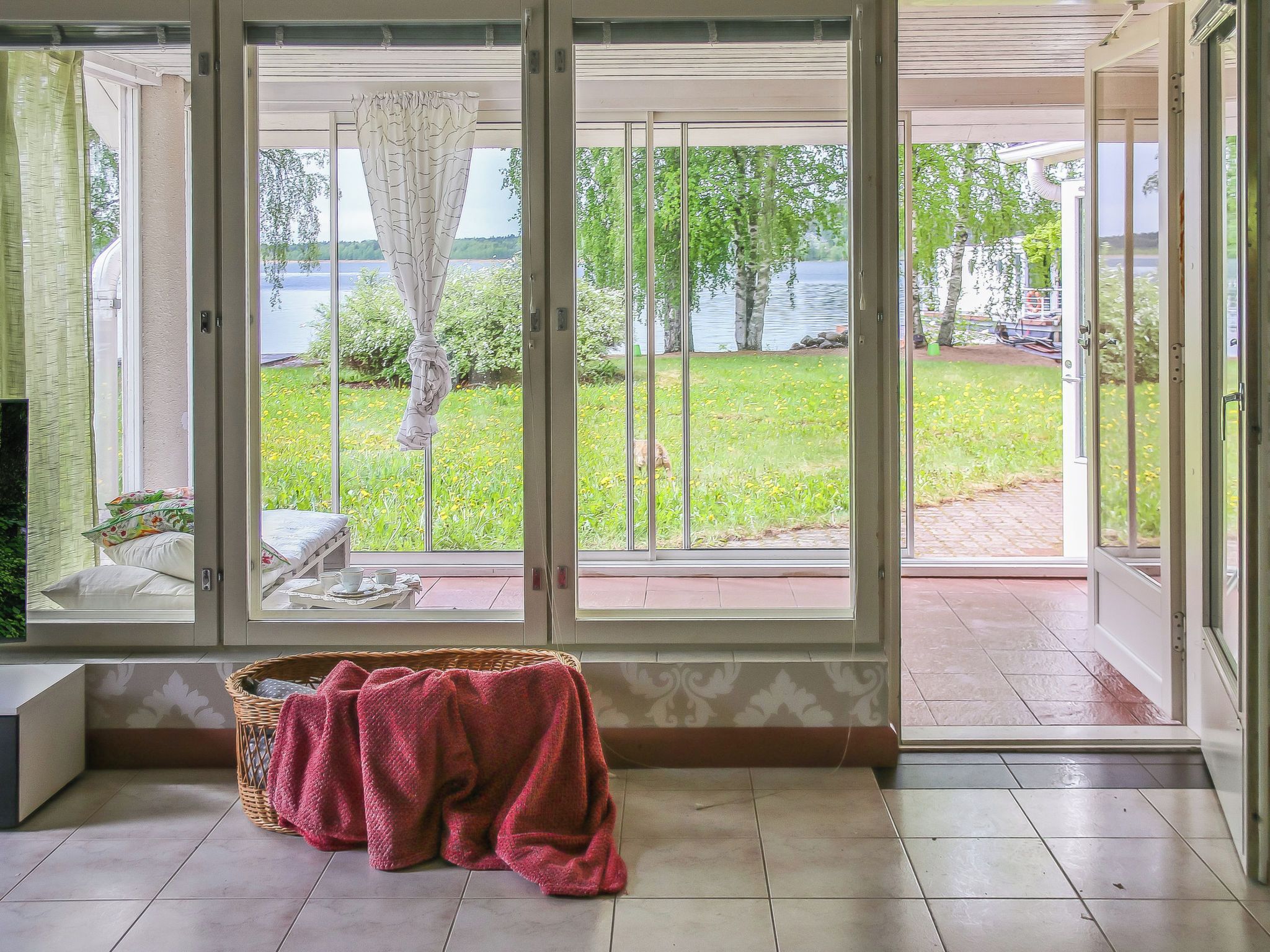 A room with a large sliding glass door leading to a garden with a view of a lake.
