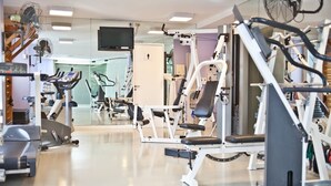 Ett gym med olika typer av träningsutrustning, en tv och en spegel.