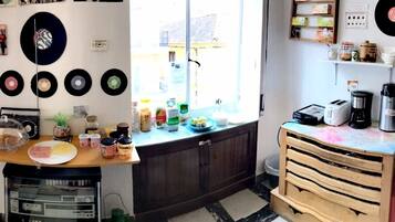 A kitchen with a wooden countertop, a coffee machine, and various kitchen items. There are vinyl records on the wall and a window with a view of the street.