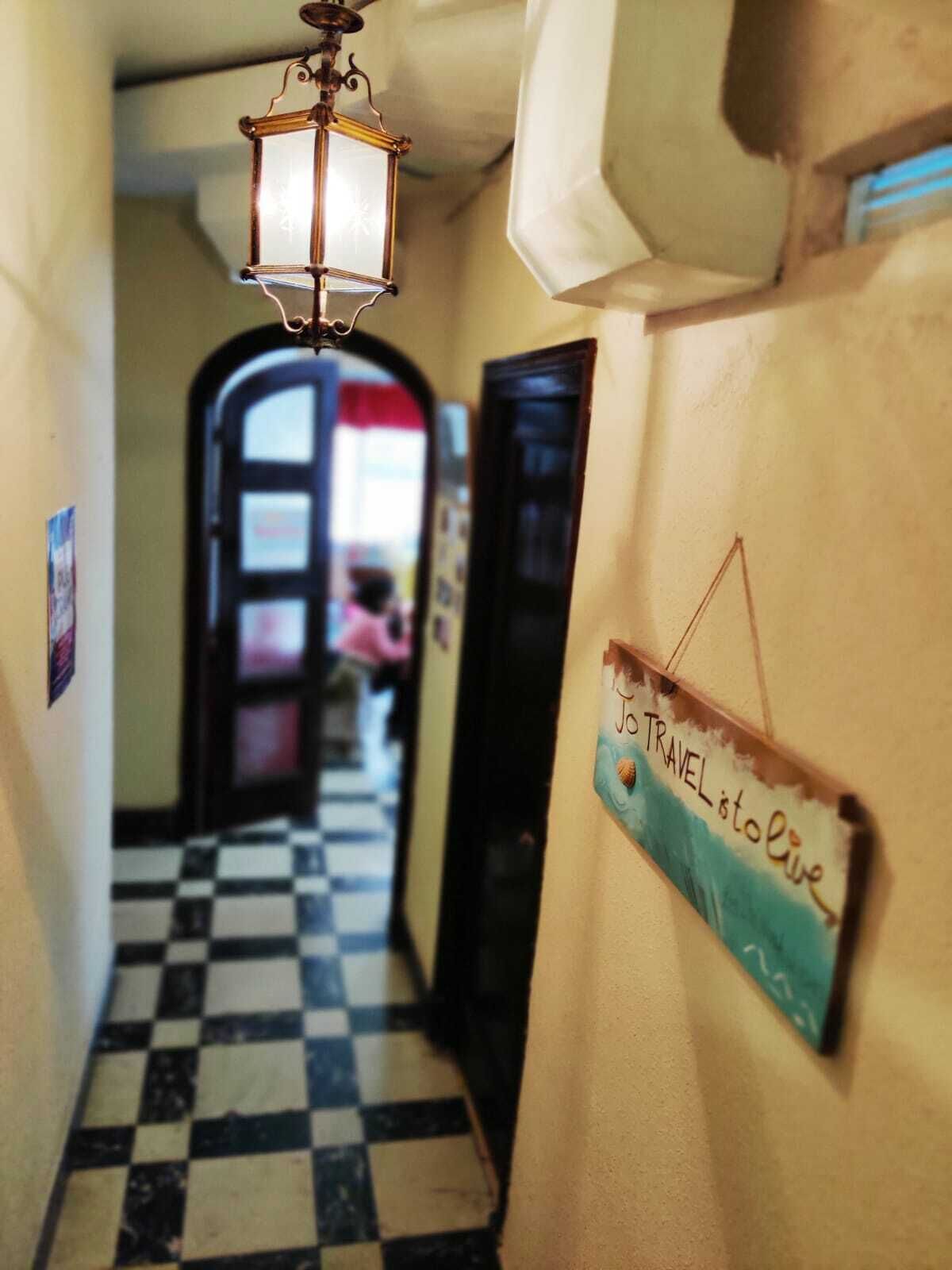 A hallway with a checkered floor, a hanging lantern, and a sign on the wall that reads "Jo's Travel is to love".