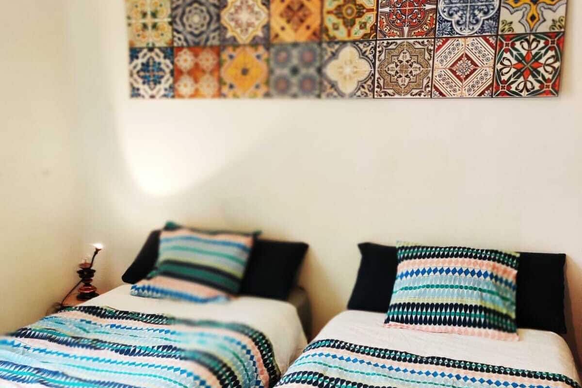 A room with two beds, each with striped bedding and pillows. A colorful tile wall hangs above the beds.