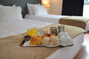 A neatly made bed with white linens and a breakfast tray on top, including croissants, pastries, and a glass of orange juice. - Hotel Girassol (Porto)