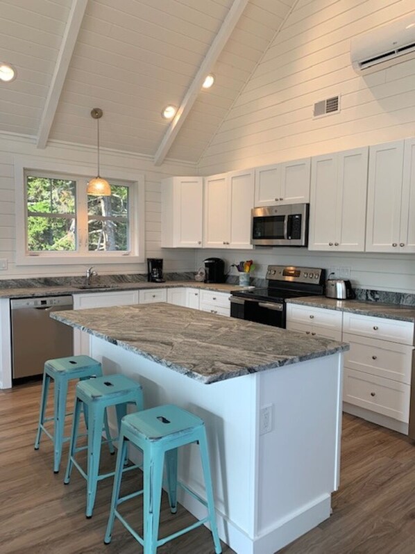 A kitchen with white cabinets, a granite countertop, a central island with stools, a window, and an air conditioning unit.