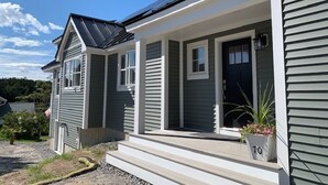 A two-story house with a covered porch, a front door, and a number '10' sign on the steps. - New Listing - Island View Cottage (Phippsburg)