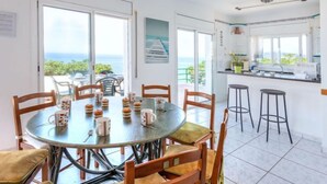 A modern kitchen with a large island, a dining area with a round table and chairs, and a view of the sea through large windows. - Don Quijote by Interhome (Llançà)