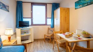 A cozy room with a bed, a TV, a dining table with chairs, and a window with curtains. - Vostok Zodiaque by Interhome (Le Corbier)