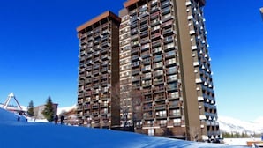 A high-rise building with multiple balconies, a ski lift in the background, and a clear blue sky. - Vostok Zodiaque by Interhome (Le Corbier)