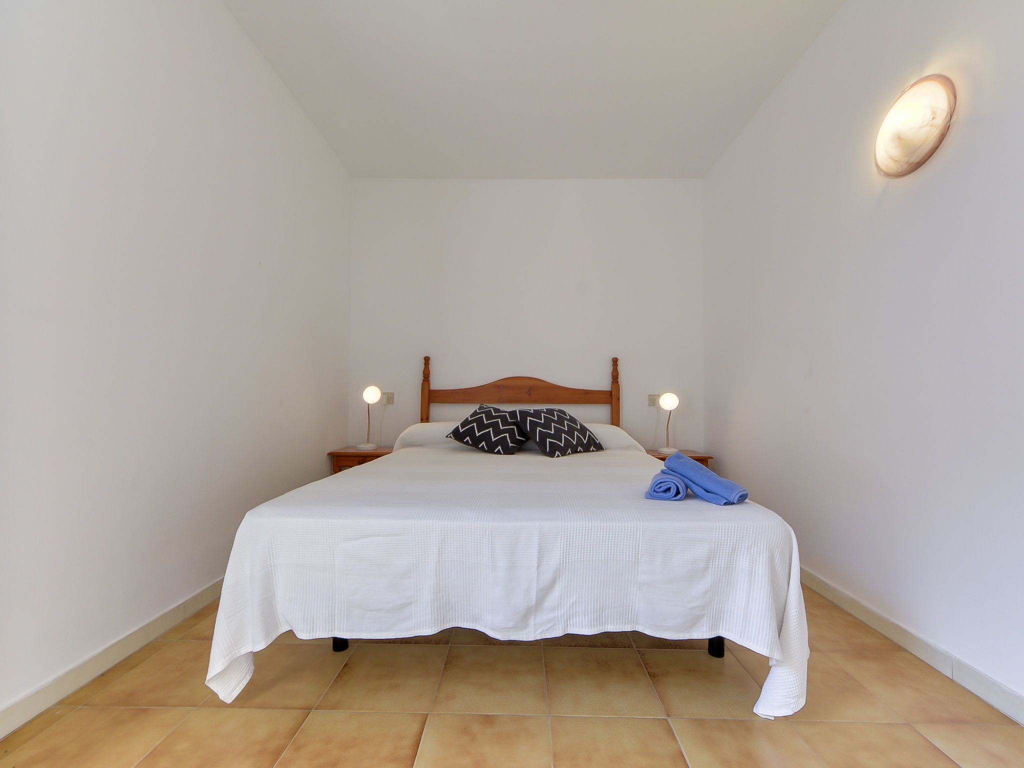 Ein ordentlich bezogenes Bett mit Holz-Kopfteil, zwei Nachttischlampen und einem gefalteten Handtuch auf dem Bett.
