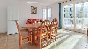 Un coin repas avec une table et des chaises en bois, un réfrigérateur blanc et un balcon offrant une vue sur les immeubles.