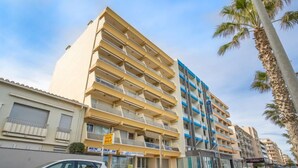A multi-story building with balconies, a parked white car, and palm trees. - Apartment Milos by Interhome (Canet-Plage)