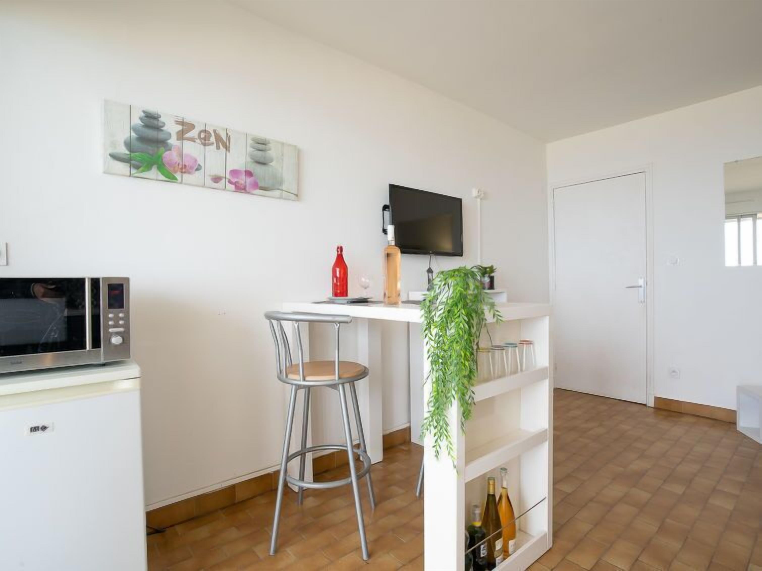 A modern kitchen with a microwave, a small refrigerator, a dining area with a chair, a table, and a TV mounted on the wall.