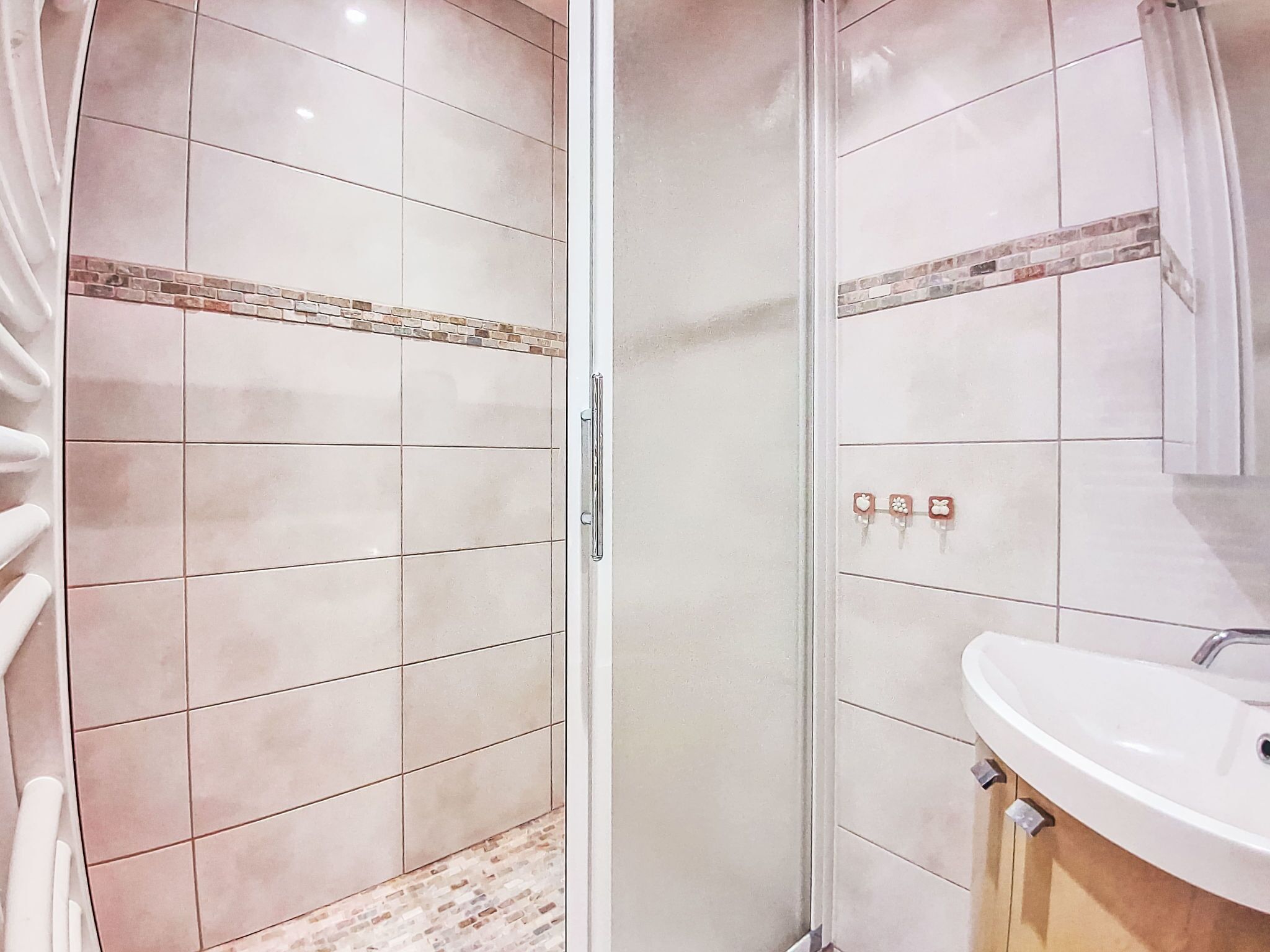 A bathroom with a glass shower enclosure, a sink, and a tiled floor.