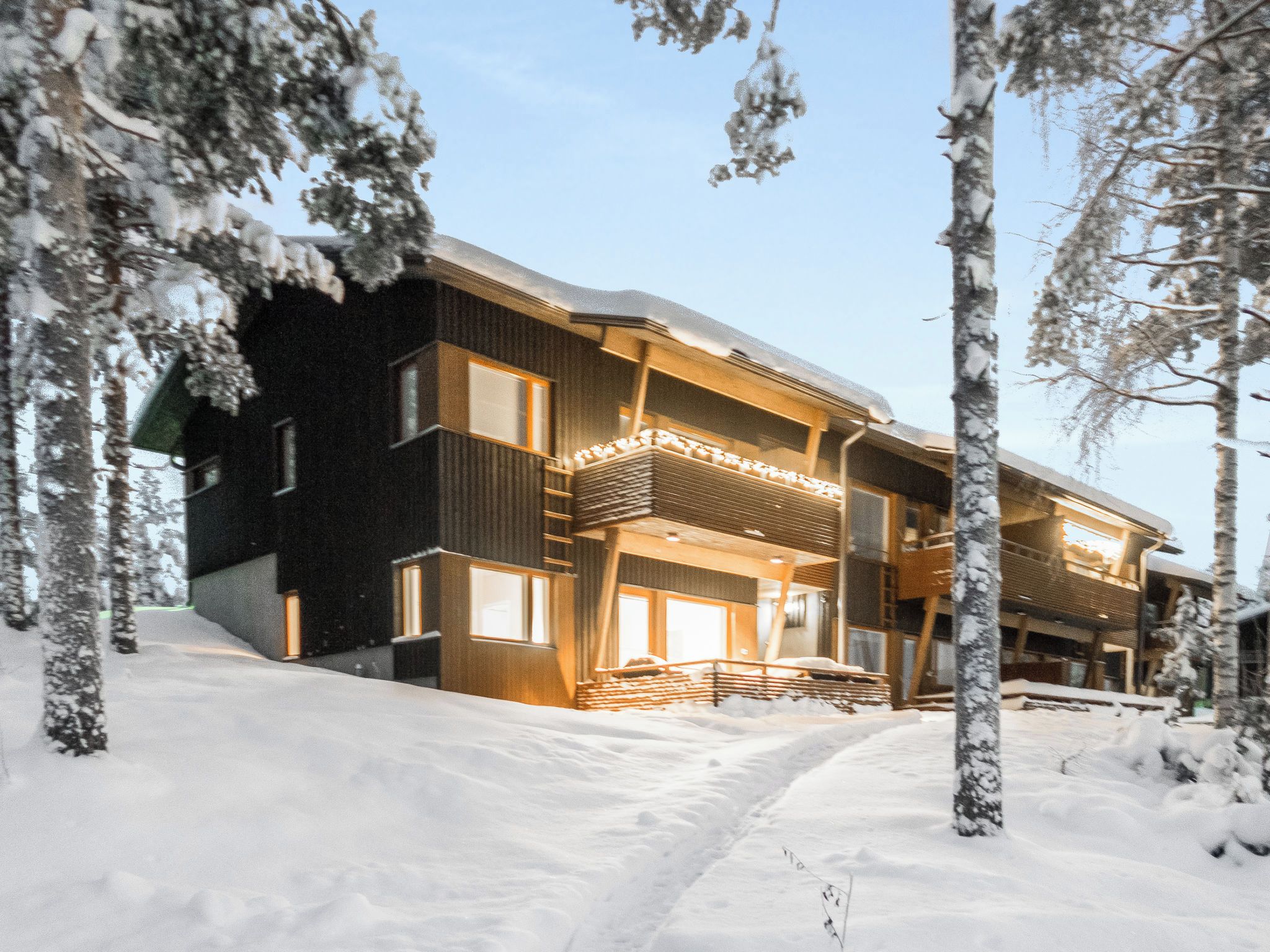 En moderne bygning med flere etager, et sneklædt landskab, store vinduer og en balkon.