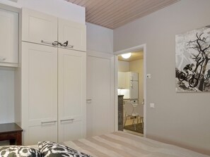 A bedroom with a large wardrobe, a bed with patterned bedding, a painting on the wall, and a doorway leading to a bathroom.