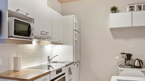 Una cocina compacta con armarios blancos, microondas, fregadero y cafetera.