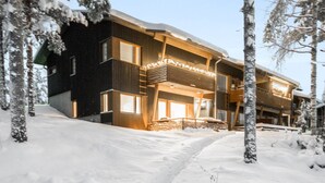 Un edificio moderno de varios pisos con un balcón, rodeado de árboles cubiertos de nieve.