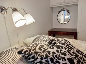 Un dormitorio con una cama, dos lámparas, un espejo y una mesita de noche de madera.