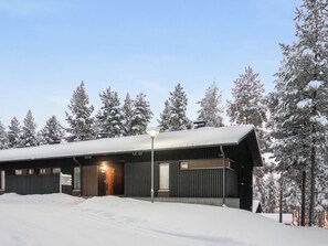 Un albergue cubierto de nieve con fachada metálica, una entrada iluminada y un cartel que indica pistas de esquí cercanas.