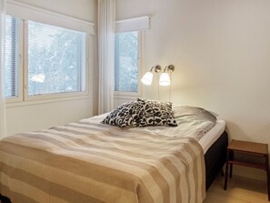 Un dormitorio con cama, dos lámparas de noche, una ventana con persianas y una mesita de noche de madera.