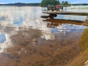 Puinen laituri, joka ulottuu kirkasvetiseen järveen, siinä on penkki ja punainen ämpäri.