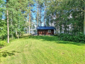 Une cabane entourée d’une zone herbeuse et de grands arbres.