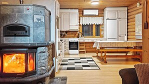 Un acogedor interior de cabaña con chimenea de piedra, mobiliario de madera y alfombra a cuadros.