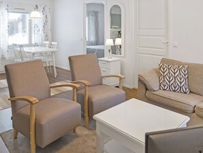 A modern living room with two armchairs, a sofa, a coffee table, and a dining area with a table and chairs.