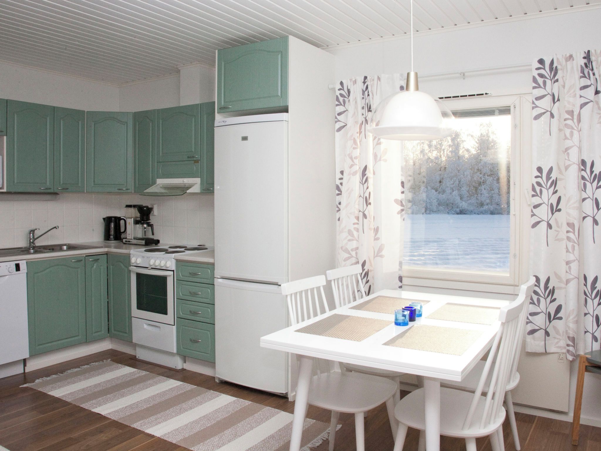 Een keuken met groene kastjes, een witte koelkast, een fornuis en een eettafel met stoelen.