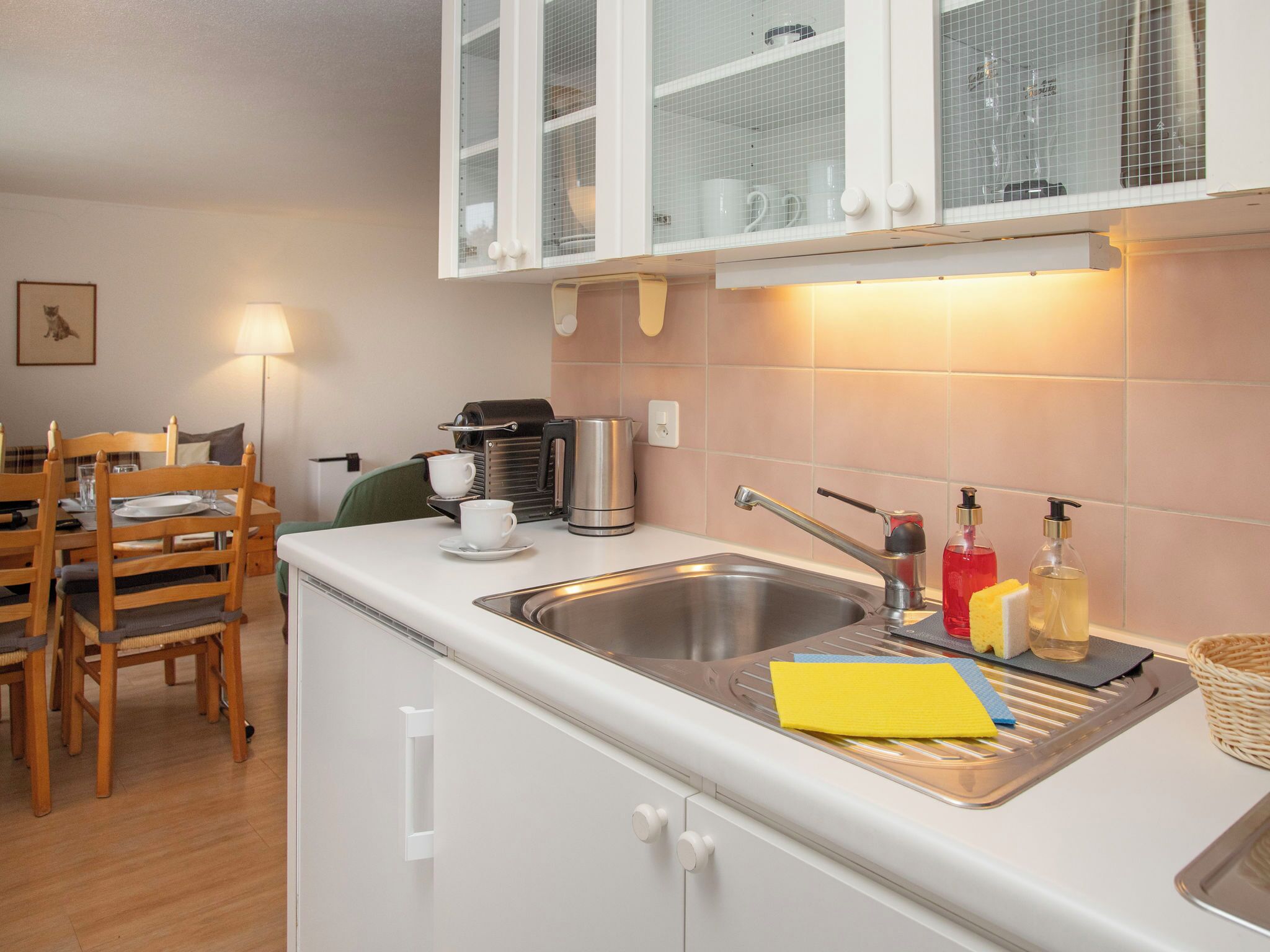 A kitchenette with a sink, a coffee machine, and a dining area with chairs and a table.