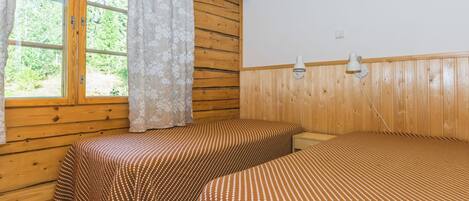 A room with two beds, wooden walls, a window with curtains, and two wall-mounted lamps.