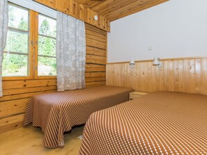 Une chambre avec deux lits, des murs en bois, une fenêtre avec des rideaux et deux lampes fixées au mur.