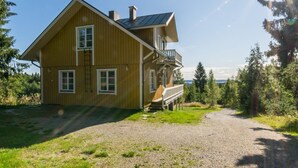 Ein zweistöckiges Holzhaus mit Balkon, einem Schotterweg und bewaldeter Umgebung.