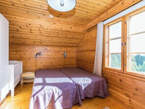 A small, wooden cabin room with a bed, a window, and a ceiling light.