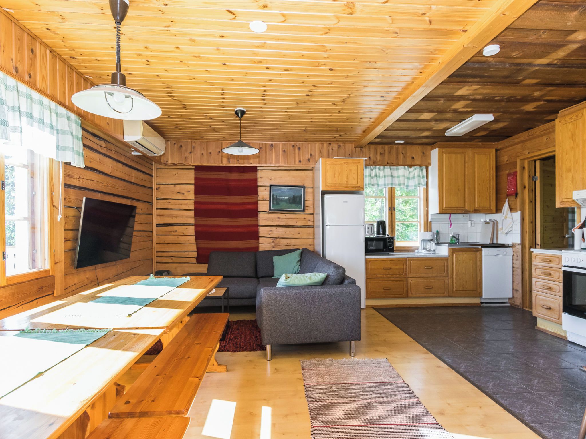 Un intérieur de chalet chaleureux comprenant un coin repas, un canapé, une cuisine et une grande fenêtre.
