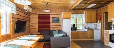 Un intérieur de chalet chaleureux comprenant un coin repas, un canapé, une cuisine et une grande fenêtre.