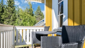 Ein Balkon mit Korbmöbeln, einem kleinen Tisch und einem Fenster mit gelben Vorhängen.