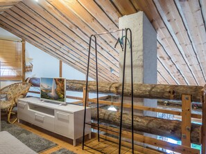 Une pièce avec un plafond en bois incliné, une armoire blanche avec des tiroirs, une chaise en osier et un banc en bois doté d’une structure métallique.