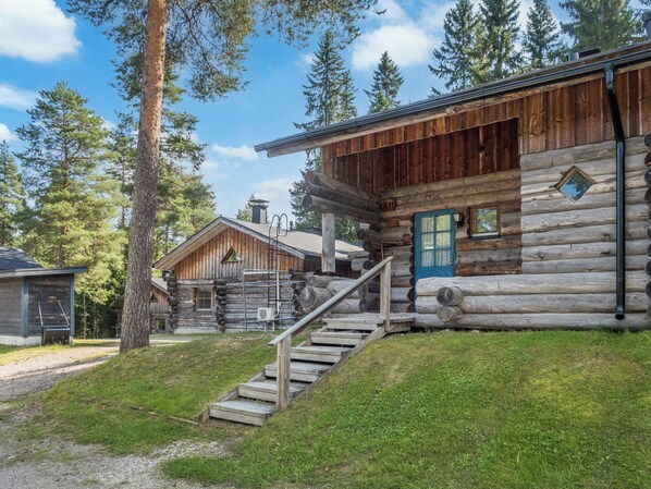 A log cabin with a wooden exterior, a blue door, and a staircase leading to the entrance.