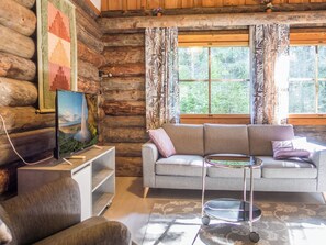 Ein Holzblockhaus-Innenraum mit einer Couch, einem Fernseher auf einem Schrank und einem Fenster mit Vorhängen.