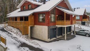 Eine moderne Blockhütte mit großer Veranda, zahlreichen Fenstern und einem geparkten Auto davor.
