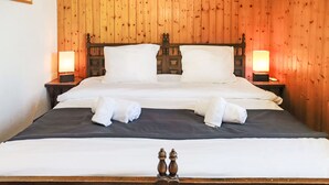 Cama doble con sábanas blancas y dos toallas enrolladas, cabecera de madera y mesitas de noche con lámparas.