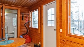 Ein Holzhütten-Interieur mit Holzbalkendecke, einer Tür mit Fenster, einem kleinen Tisch mit blauer Unterlage und einer roten Tasche auf dem Boden.