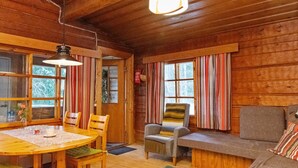 Ein gemütliches Blockhauss-Interieur mit einem Holzesstisch, Stühlen, einer Couch und einem Fenster mit gestreiften Vorhängen.