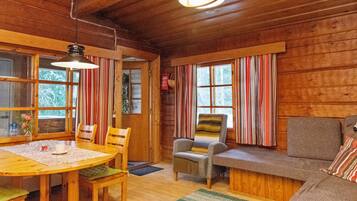 A cozy cabin interior with a wooden dining table, chairs, a sofa, and a window with striped curtains.