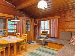 A cozy cabin interior with a wooden dining table, chairs, a sofa, and a window with striped curtains.